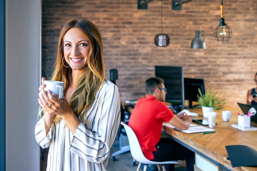 Happy business woman looking at the camera drinking coffee.
